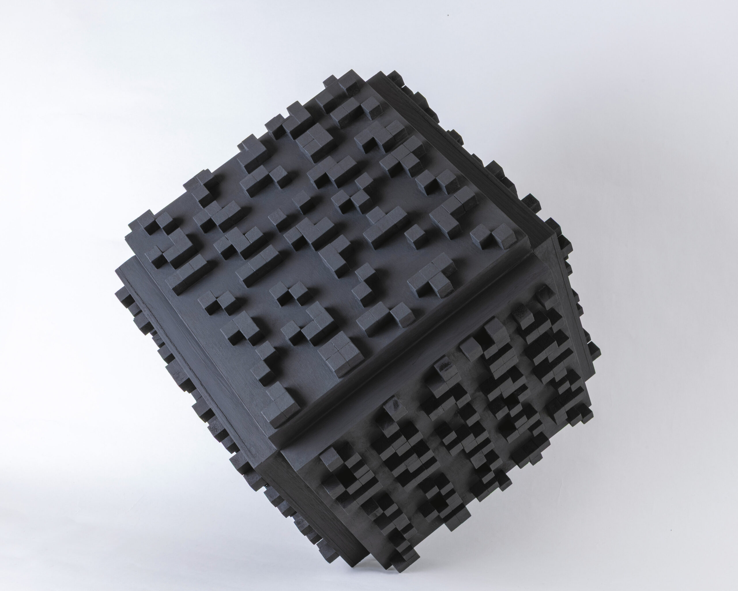 Un cube noir repose sur une surface blanche sur un de ses sommets. Des petits cubes noirs ont été disposés sur les faces du cube afin de créer un texte en braille.