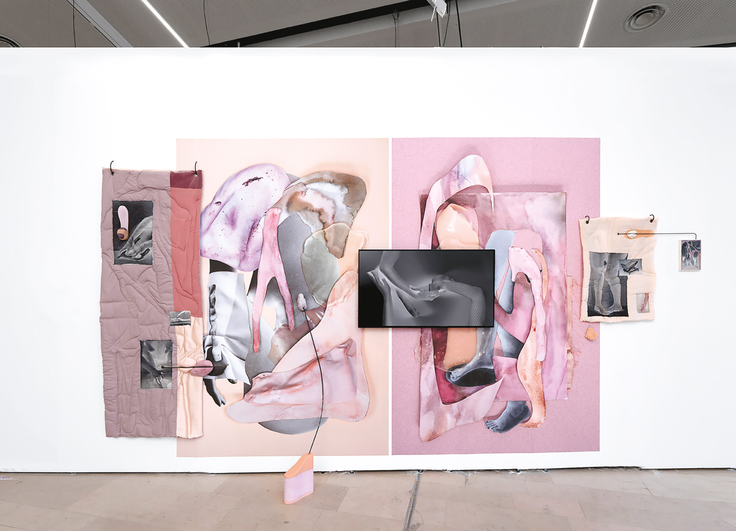 Sur un grand mur blanc, une œuvre composée de quatre panneaux est installée. Le panneau de gauche est constitué de quatre morceaux de tissus de différentes teintes de rose. Des photographies de mains et de corps féminins sont accrochées sur les textiles. Une partie du panneau de gauche est légèrement disposé sur le panneau qui se trouve à sa droite. Ce panneau comporte de grandes formes arrondies texturées dans les teintes de roses pâles sur un fond rectangulaire beige. Le panneau à sa droite est similaire, les teintes de roses sont plus foncées et il est possible de distinguer deux jambes à travers les grandes formes arrondies. Un film négatif de trois mains est entre les deux panneaux. Le dernier panneau à droite est plus petit. Il s'agit d'un textile beige avec trois photographies monochromes. Les photographies représentent, individuellement, des jambes, une civière et un bras.